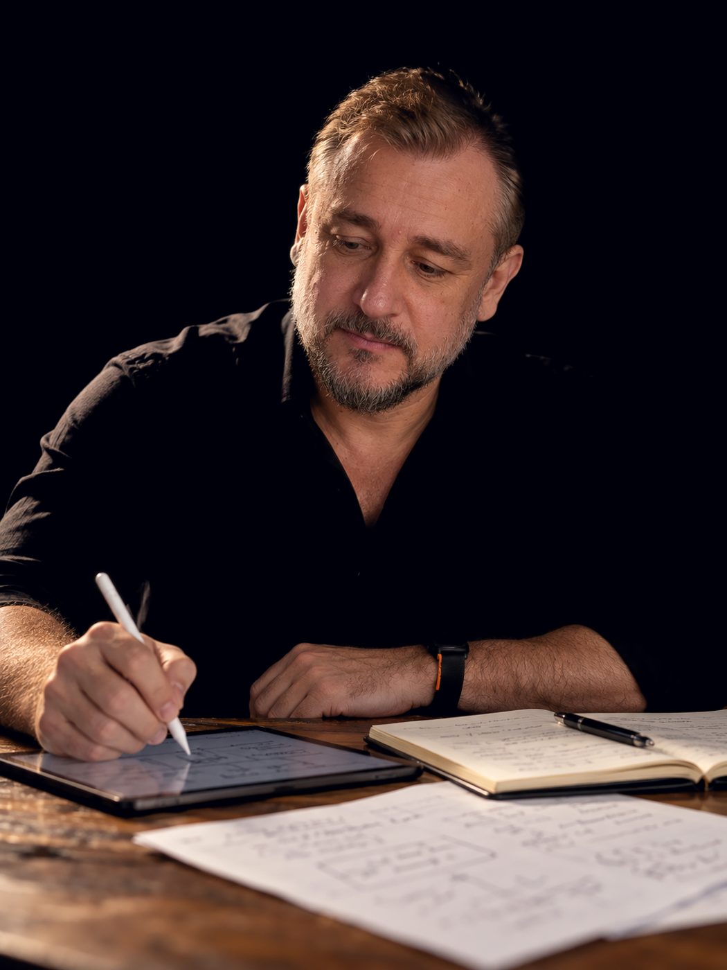 Beto Canuto escrevendo à mesa, com caderno e tablet.